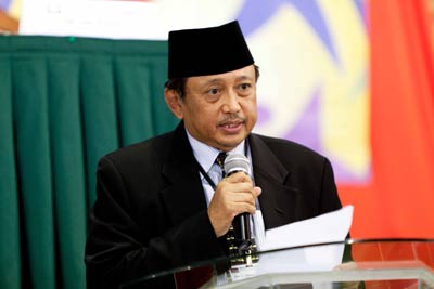 A man in a suit representing faith leaders speaking into a microphone at the Global Peace Convention, promoting social cohesion.