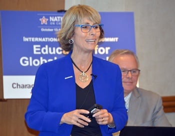 A woman in a blue blazer speaking at a podium with a banner reading