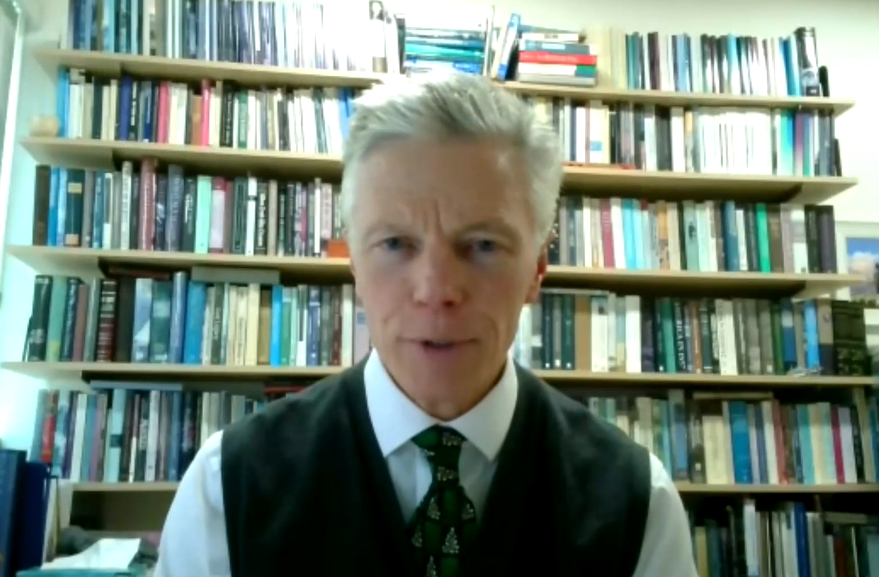 A man in a vest and tie standing in front of a bookshelf, embodying freedom of conscience.