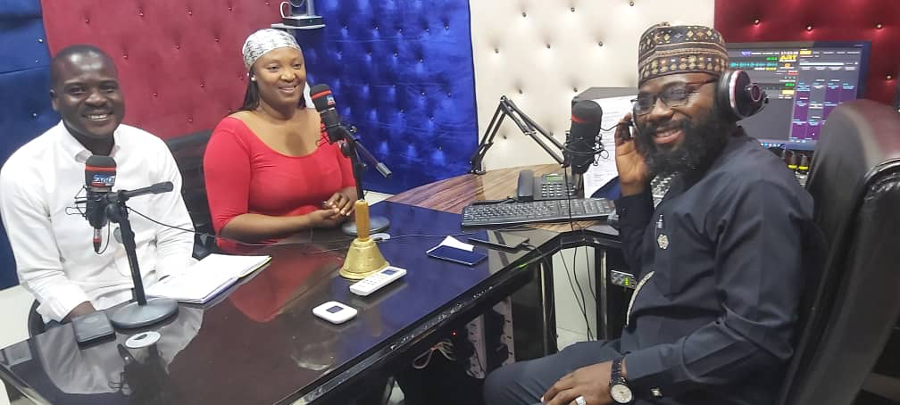 Three people sitting at a table in a radio studio exemplify peaceful coexistence.