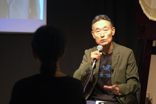 The Peace Design Forum: Peacebuilding Together in Asia is showcased as a man confidently speaks into a microphone in front of a group of people.