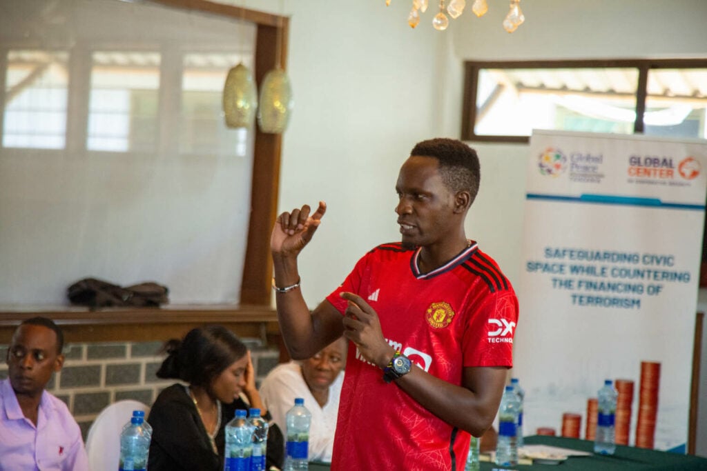 A man is giving a presentation on the GPF Tanzania program, focusing on safeguarding civic space, to a group of people.