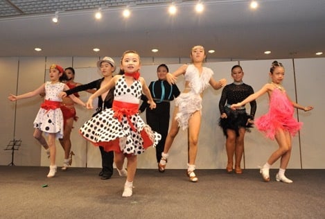 A multicultural group of children are dancing on a stage at a Family Festival, showcasing different cultures.