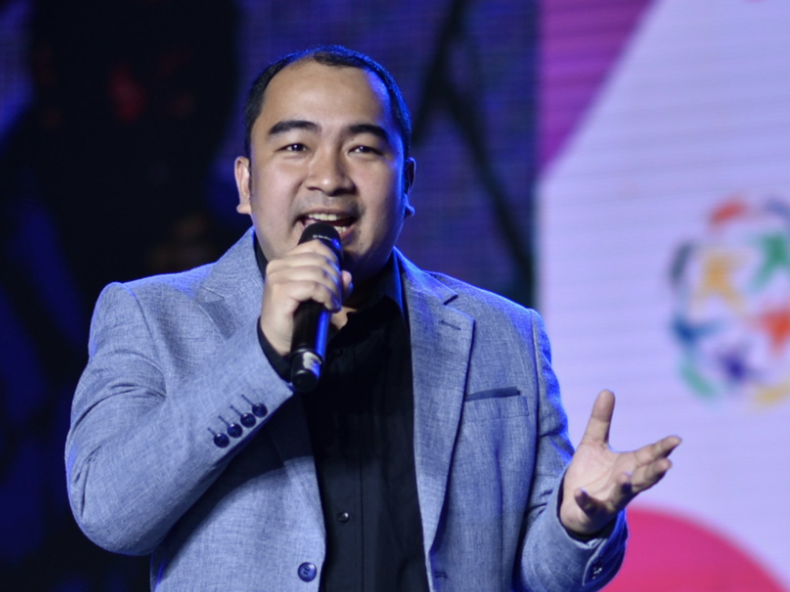 At the global peace youth festival, a man confidently holds a microphone in front of a captivating stage.
