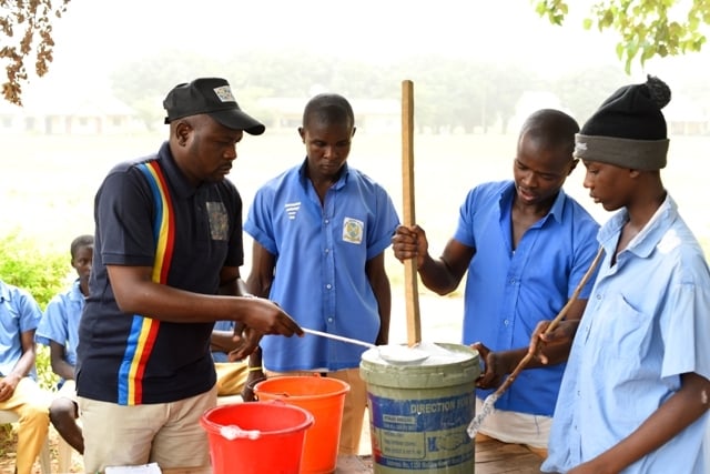 A group of youths in blue shirts are participating in a skills acquisition program, working together on a bucket.