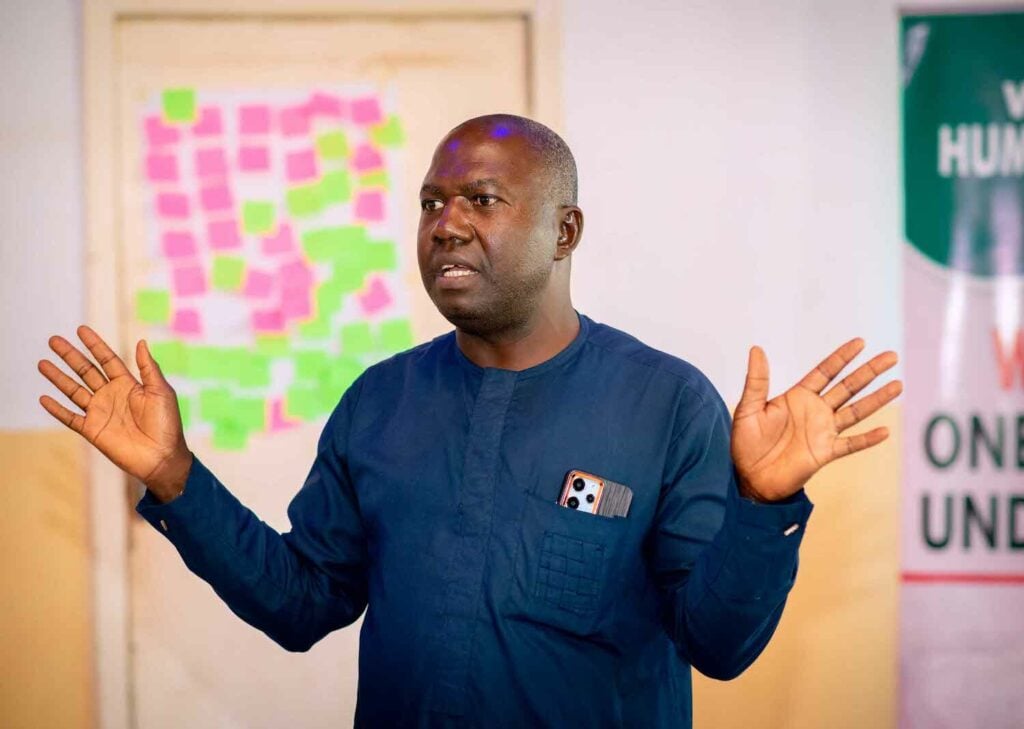 A man with his hands out in front of a room, leading a peacebuilding workshop in Nigeria.