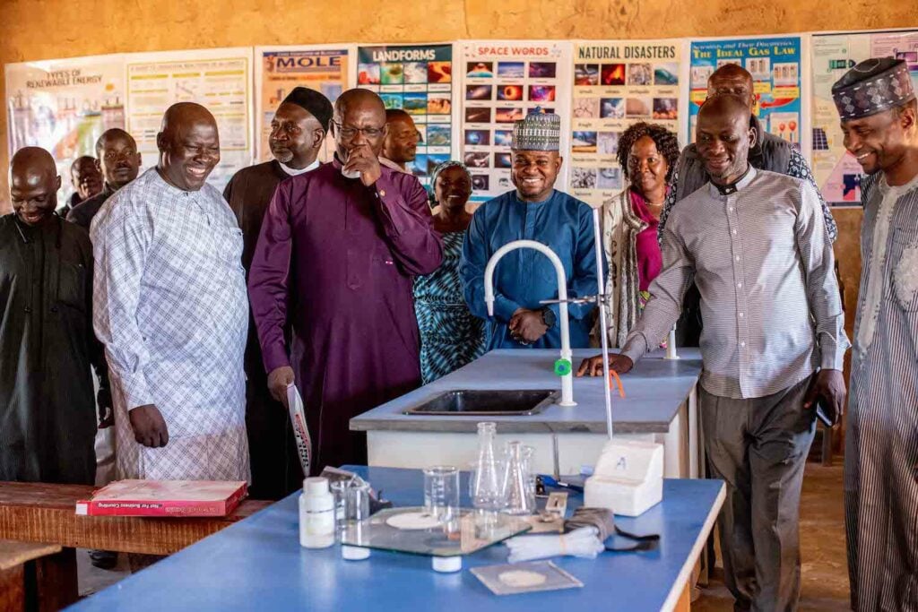 A group of people standing around a table in a classroom, fostering social cohesion.