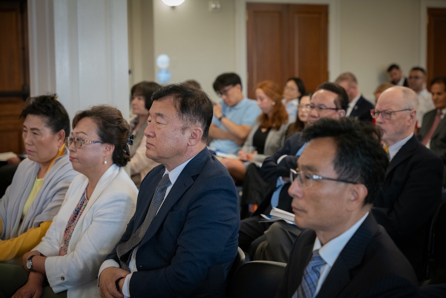 A group of people seated and attentively watching a presentation in a conference room setting at the International Forum on One Korea.