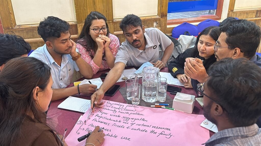 A group of innovative leaders, including Nepali youth, sit around a table discussing various points written on a large pink sheet of paper.