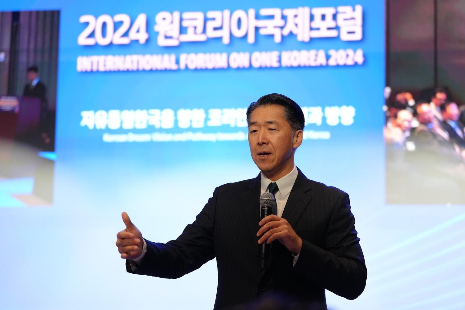 A man in a suit is speaking into a microphone on stage at the