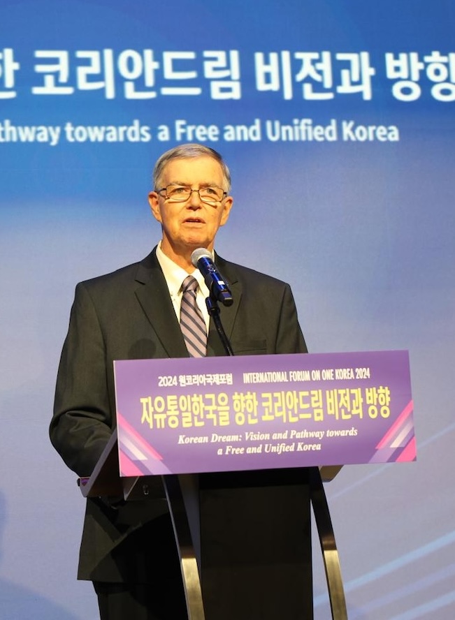 A man in a suit speaks at a podium during the 2024 International Forum on One Korea, with a backdrop that reads