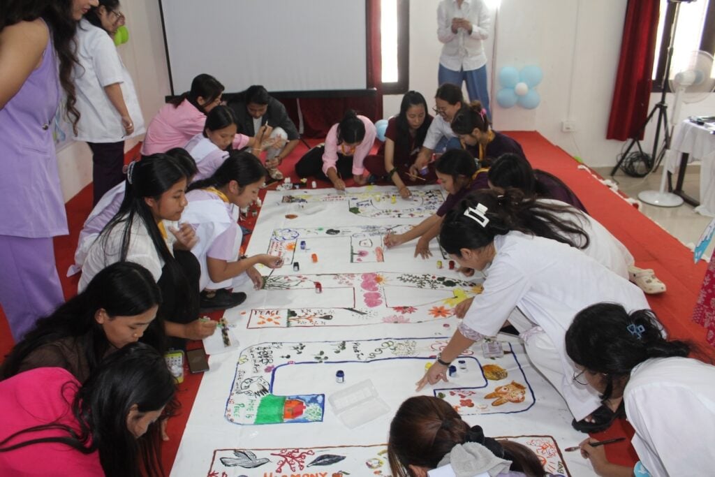 A group of people, engaged in leadership training, crouches on the floor, collaboratively working on colorful drawings or diagrams on large sheets of paper.