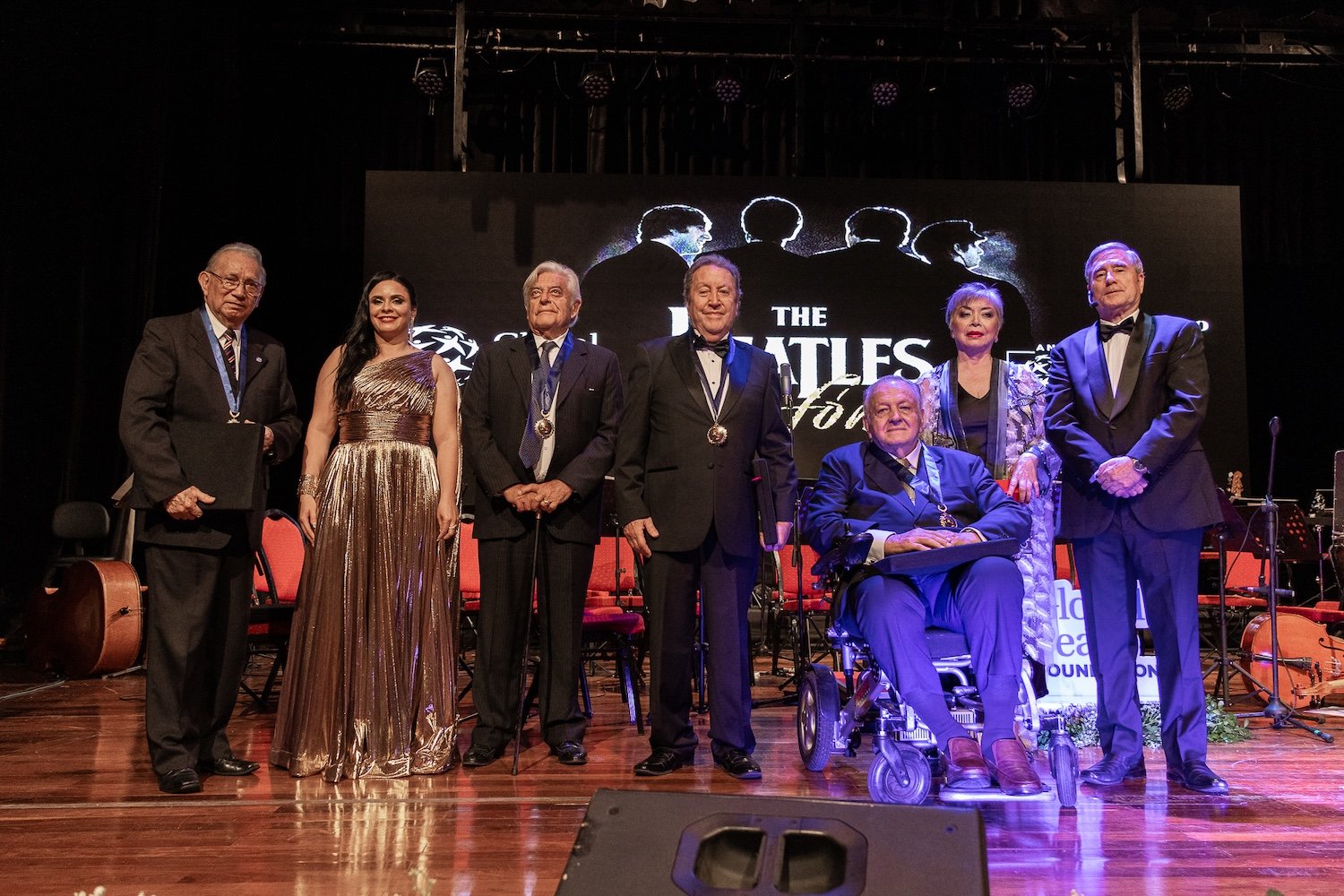 Seven people in formal attire pose on a stage in front of a