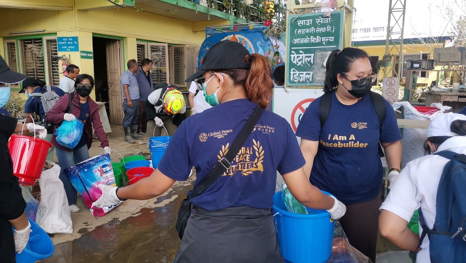 Volunteers wearing masks sort cleaning supplies outside a building in Kathmandu. Some, showcasing their resilience with shirts reading