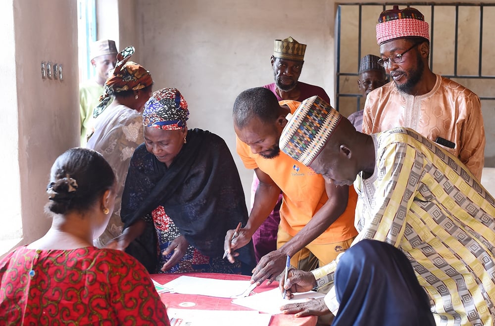 People gathered around a table, signing documents dedicated to sustainable peace in a room with natural light.