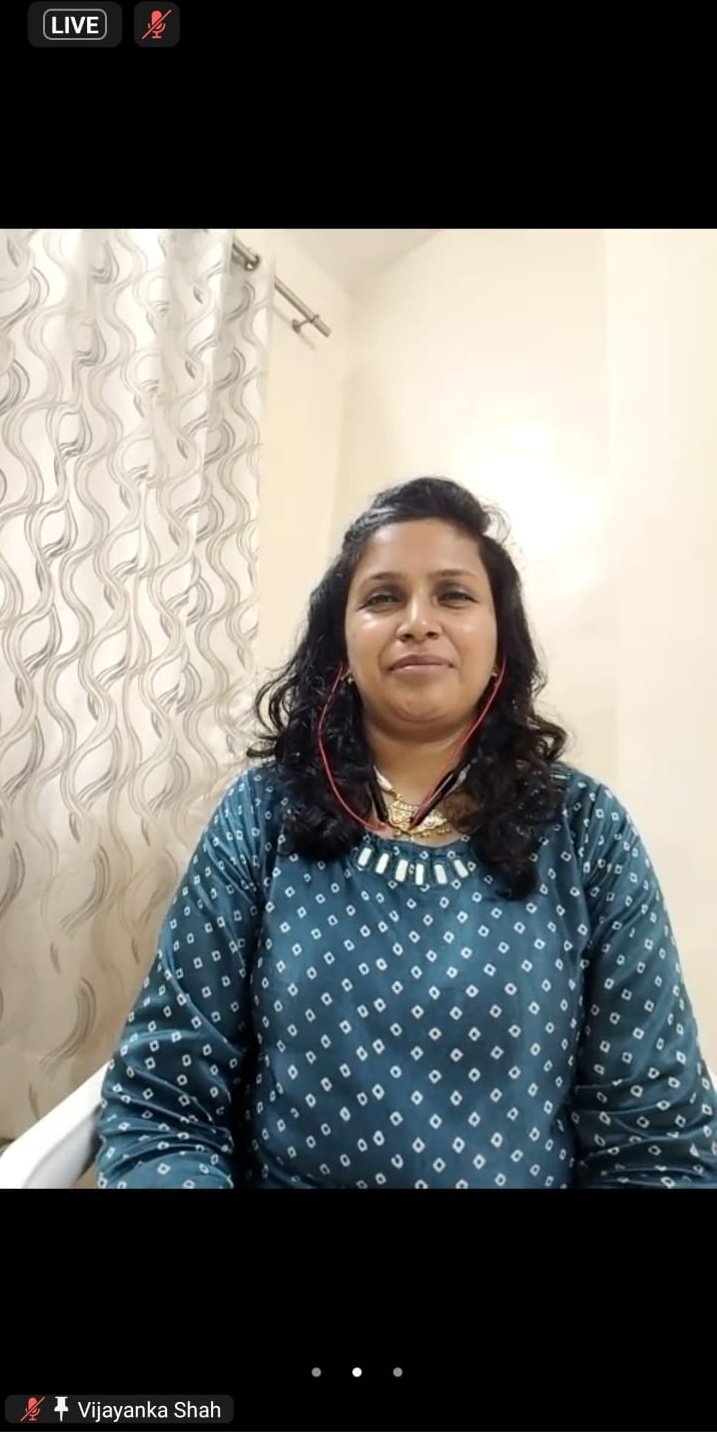A person with long hair and a blue patterned sweater sits in a room with a floral curtain behind them, reflecting on World Mental Health Day 2024.