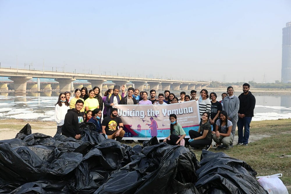 A group of people stands together by the Yamuna Ghat, proudly holding a