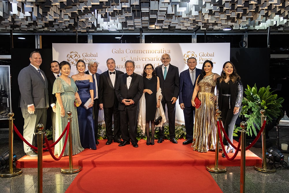 A group of twelve people dressed in formal attire pose on a red carpet at an event with a