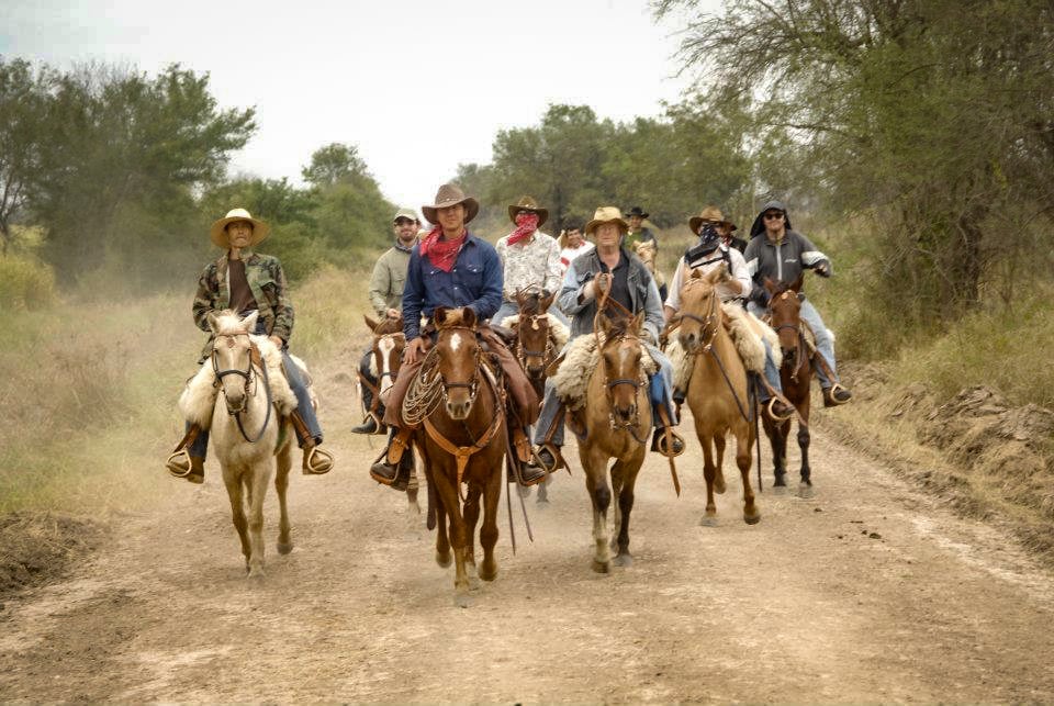 A group of people riding horses on a dirt path in an outdoor setting with trees in the background.