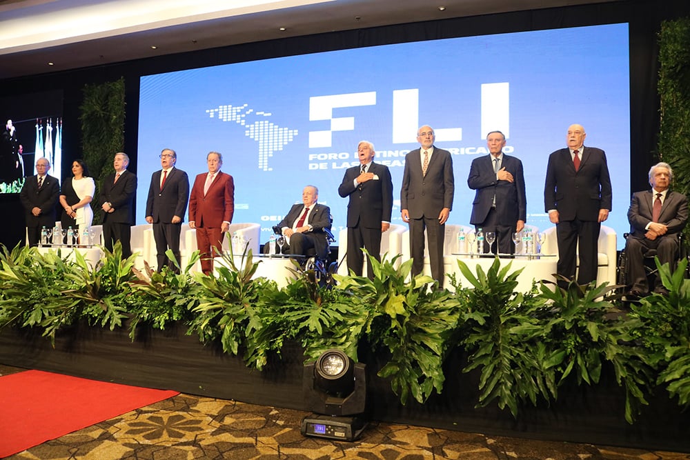 A group of nine people stands on a stage in front of a large sign that reads