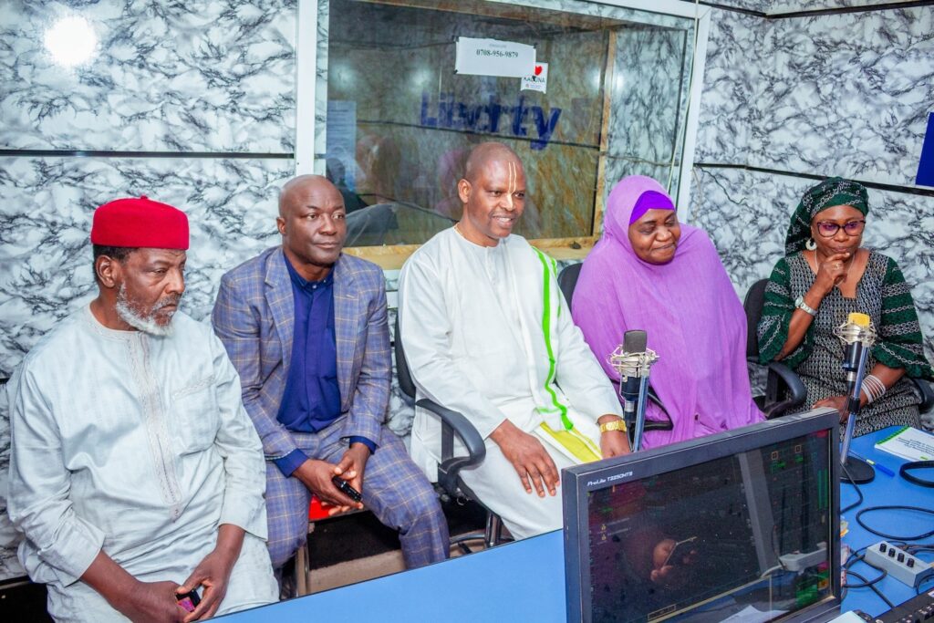 Five people are seated in a radio studio with microphones, looking towards the camera, ready to discuss World Interfaith Harmony and how interfaith collaboration can foster understanding across communities.