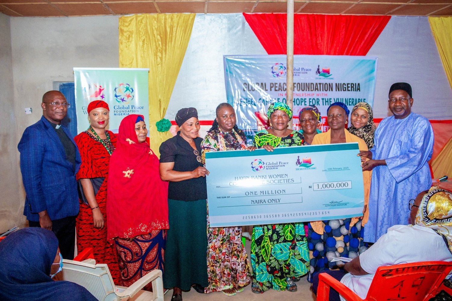 A group of people posing indoors with a large ceremonial check for one million naira, presented by GPF Nigeria. A banner advocating women empowerment is visible in the background.