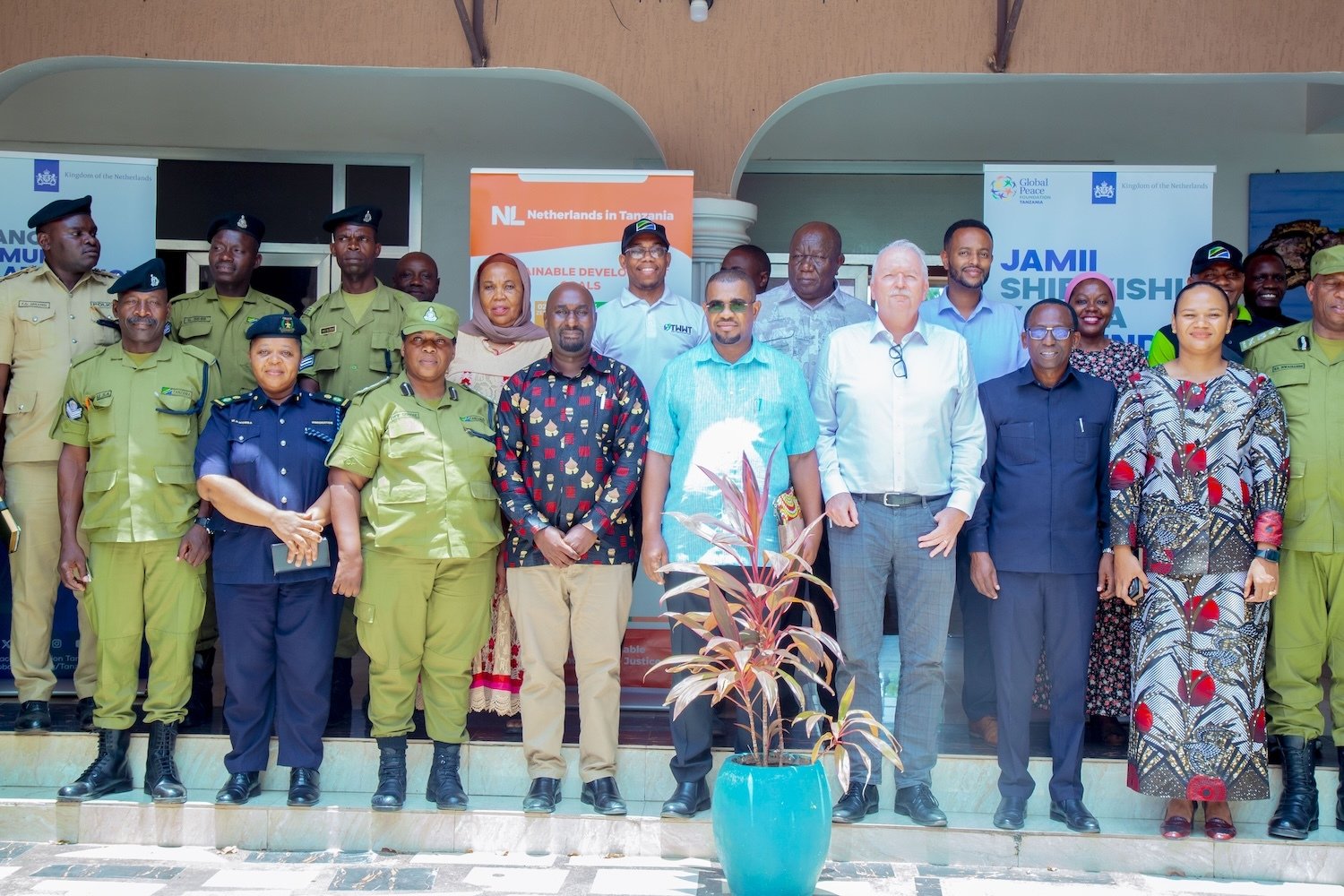 A group of individuals, including uniformed officers and civilians, stand for a photo in front of banners and a building entrance, showcasing their commitment to community collaboration in Southern Tanzania.