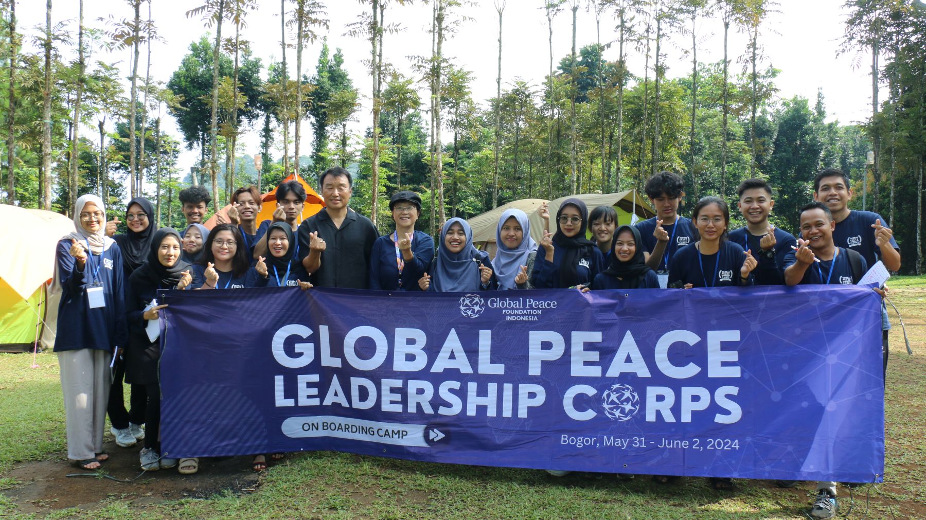 A group of young adults and a leader, representing Global Peace Leadership Corps Indonesia, stand outdoors behind a banner that reads "Global Peace Leadership Corps On Boarding Camp, Bogor, May 31 – June 2, 2024.