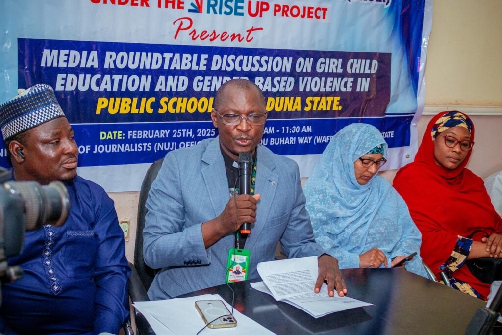 A group of people are seated at a table during a media roundtable on girl child education and gender-based violence in public schools, Nigeria. A man is speaking into a microphone.