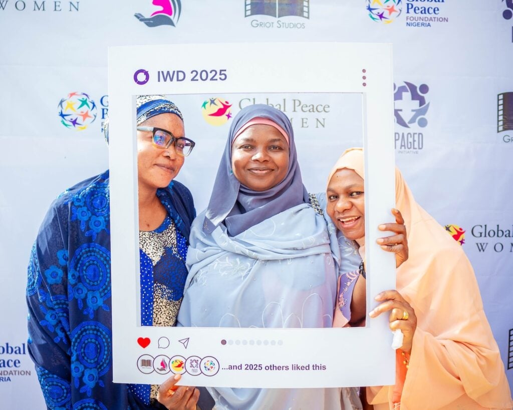Three women in colorful hijabs pose together behind a large Instagram photo frame prop labeled