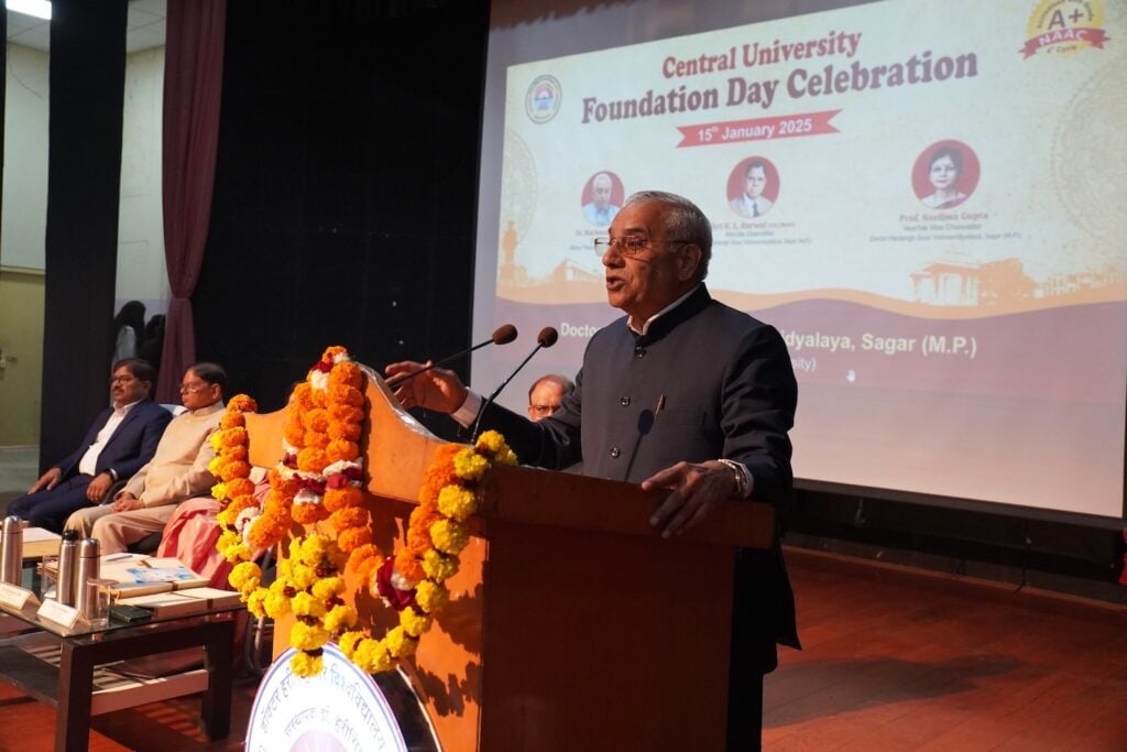 At the Central University Foundation Day Celebration, a speaker at the podium discusses spreading peace, as people seated on stage listen attentively. The backdrop highlights a presentation honoring Vishwavidyalaya's legacy and Dr. Harisingh Gour's impactful contributions.