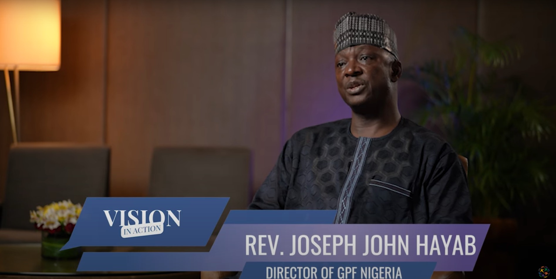 Rev. Joseph John Hayab, Director of GPF Nigeria, sits indoors and speaks during an interview about promoting unity in Nigeria. The text "Vision in Action" appears on the screen.