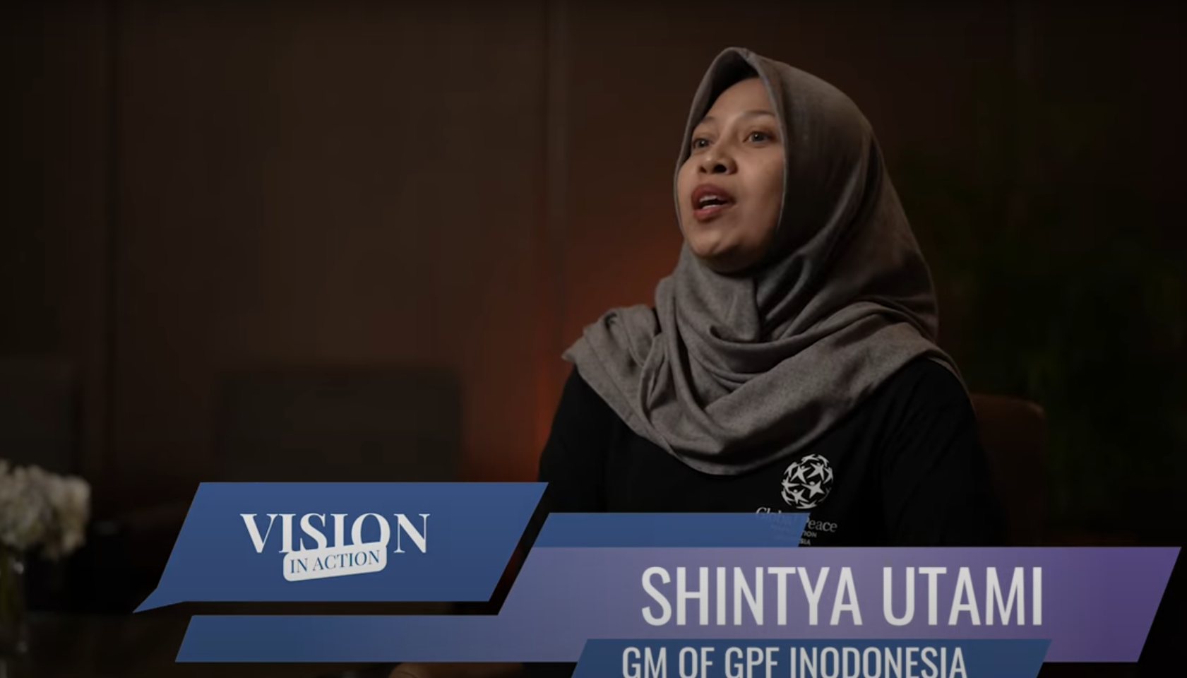 A woman in a headscarf speaks in an interview setting; on-screen text reads "VISION IN ACTION" as she discusses empowering Indonesian youth and upholding Pancasila. "SHINTYA UTAMI GM OF GPF INDONESIA" appears onscreen.