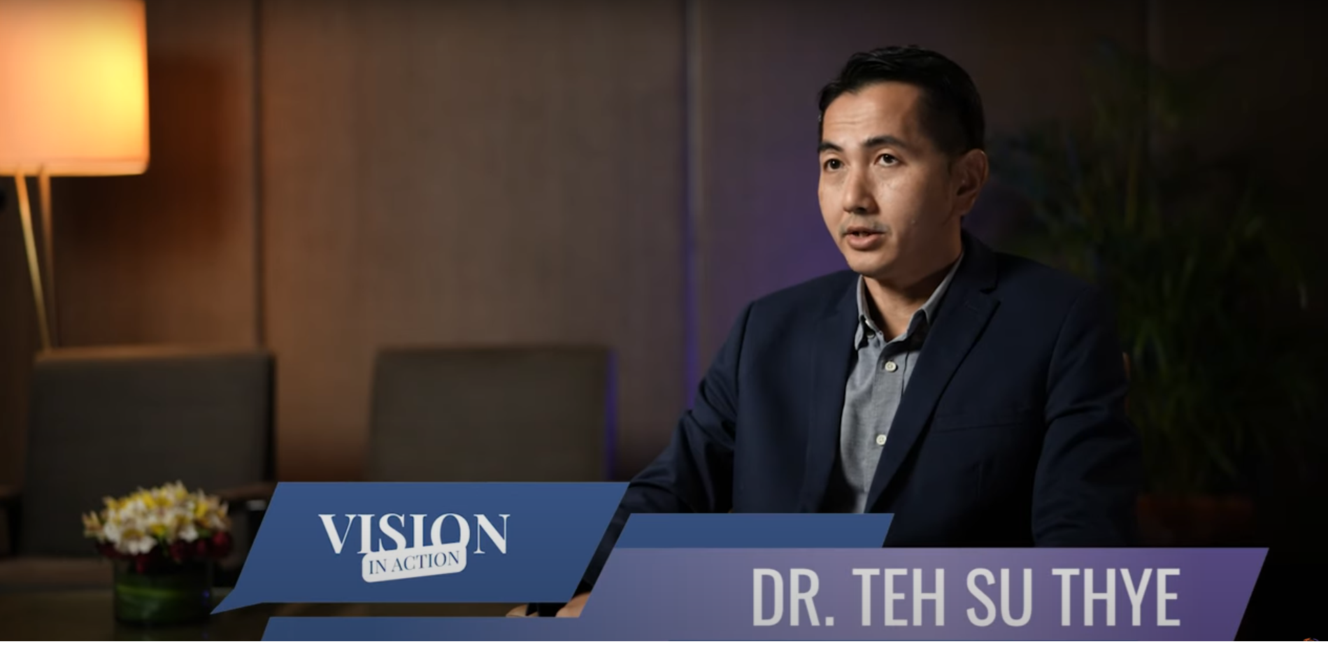 A man in a suit sits for an interview in a dimly lit room; a banner reads "VISION IN ACTION" and "DR. TEH SU THYE," highlighting efforts to ensure no one is left behind while engaging rural communities.