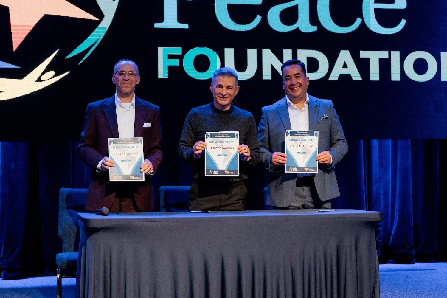 Three men in suits stand behind a table, each holding a certificate, with a large "Global Peace Foundation" sign displayed behind them on stage, celebrating shared commitments to religious freedom and family values.