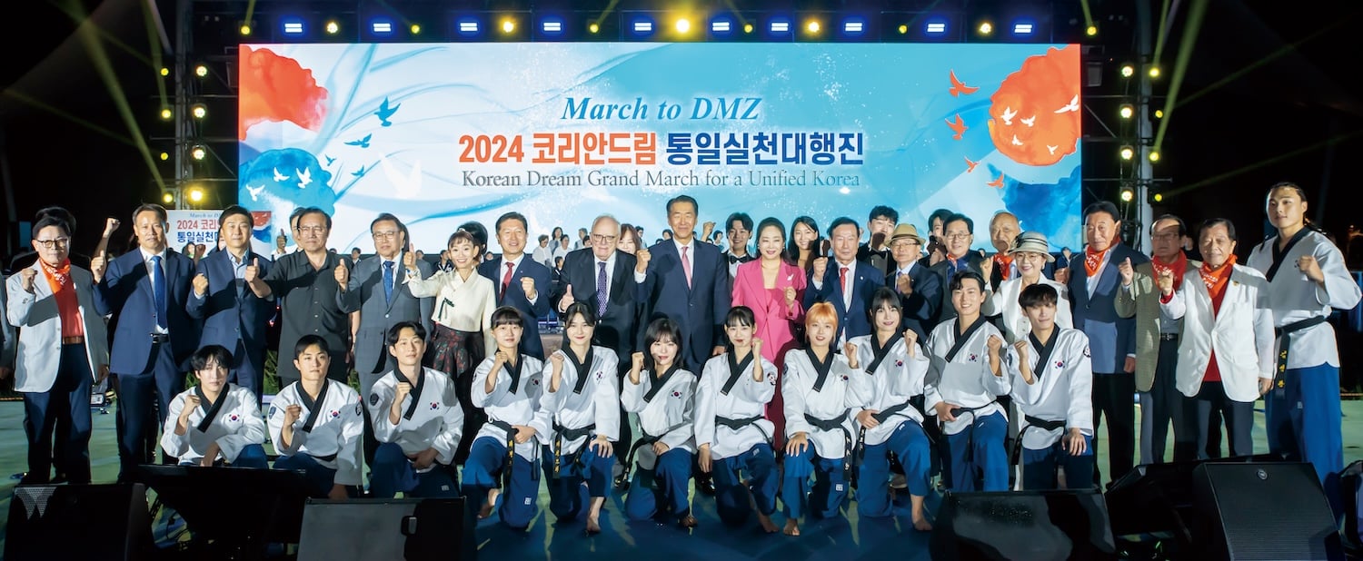 A large group of people, including officials and performers in uniforms, pose together onstage in front of a